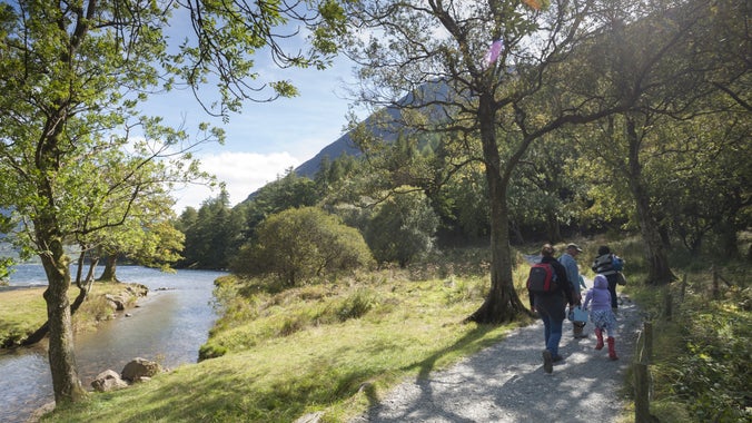 A family walk along the path by the shores of Buttermere on a sunny day with views out to the fells beyond